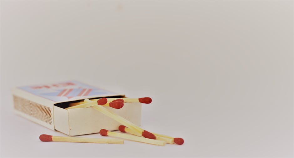 A small open cardboard box lying on a white surface, filled with several wooden matches featuring red-tipped heads. Some matches are arranged outside the box, scattered on the surface. The background is plain and neutral, highlighting the matches and box clearly. This setup is part of a house removal or packing process, illustrating careful handling of small items during a home relocation. The image emphasizes the importance of organized packing materials and the process of loading essential items into a moving vehicle, consistent with professional removals services such as those provided by Man and Van Leyton. The lighting is soft and even, ensuring all objects are visible with clear detail, suitable for an online page discussing tips for house removals or furniture transport.