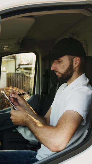 A man wearing a black cap, white polo shirt, and jeans is crouched on the pavement outside a property, surrounded by open cardboard boxes filled with packing materials, during a home relocation proces